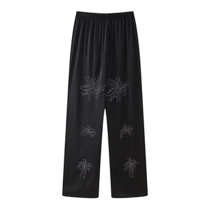 Detail of black wide-leg trousers with elegant floral embroidery and silky texture