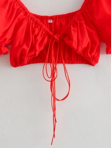 Close-up of red crop top with flared sleeves and lace-up drawstring neckline detail