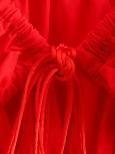 Close-up of red textured fabric featuring elastic pleats and an intricate decorative knot