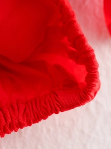 Detail of red off-shoulder top showing elastic cuffs and pleated fabric texture