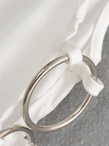 Detail of silver metal ring accessory on white slim-fit dress fabric with smooth texture