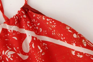 Détail du tissu en mousseline rouge avec plissage délicat et motif floral doré chic