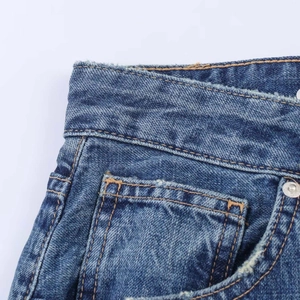 Detail of blue balloon jeans featuring orange stitching, metal rivets and raw hem waist