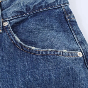 Macro detail of dark blue denim pocket with silver rivet and vintage wash texture