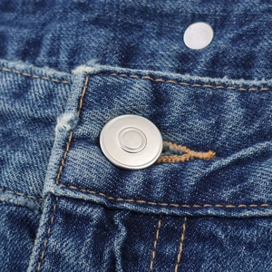 Close-up of matte silver metal button and yellow stitching on washed denim jeans