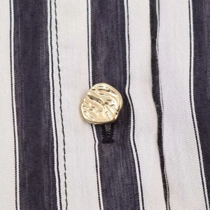 Detailed close-up of a decorative gold irregular button on a black and white striped dress