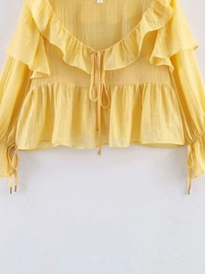 Detail of yellow chiffon blouse with ruffled neckline and delicate drawstring tie design