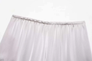 Detailed view of elastic waistband on silver satin shorts with smooth silk-like texture