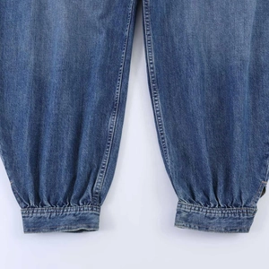 Detail of dark blue denim pants showing pleated balloon leg cuffs with metallic buttons