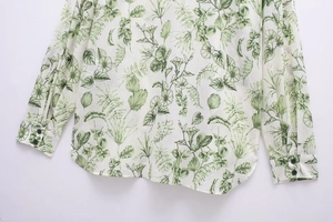 Détail d'imprimé floral vert sur chemise blanche avec boutons noirs et ourlet arrondi