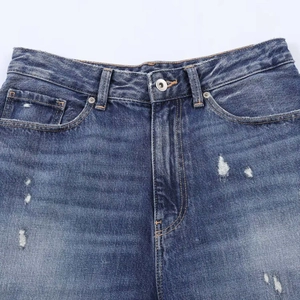Close-up of loose ripped denim jeans featuring metal button and washed finish detail