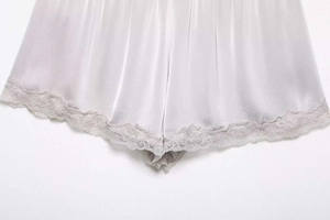 Detailed close-up of silver satin fabric with intricate lace trim on the hemline
