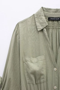 Detail of light green linen blend dress with V-neck, buttons, and pleat textures