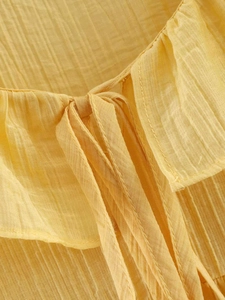 Close-up of ruffled neckline and drawstring ties on a yellow textured chiffon blouse