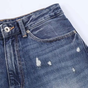 Detailed close-up of dark blue washed denim jeans with distressed holes and metal hardware