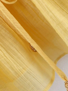 Detail of yellow pleated chiffon fabric with an elegant golden hollow spherical pendant