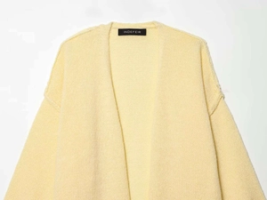 Detail view of the chunky knit texture and brand label on a yellow cardigan sweater