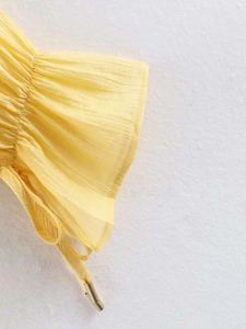 Detail of yellow chiffon sleeve with ruffled cuffs and elegant gold drawstring ends