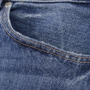 Macro shot of loose denim jeans showing distressed front pocket with vintage wash texture