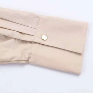 Close-up of pleated beige shirt cuff featuring a decorative round gold button detail