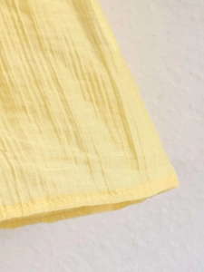 Detailed close-up of light yellow pleated chiffon fabric with neat hemmed edges