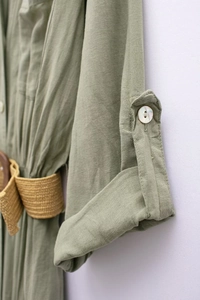 Close-up of olive green linen dress fabric with shell button and woven straw belt detail