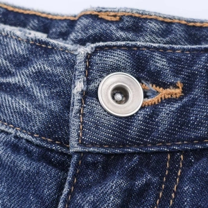 Close-up of deep blue denim texture with silver metal button and precise stitching details