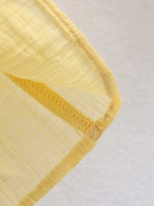 Macro shot of yellow chiffon blouse detailing neat stitching and sheer textured fabric
