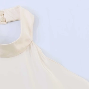 Close-up of cream halter top neckline featuring two matching back buttons and satin texture