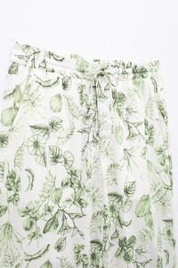 Détail d'un pantalon d'été blanc avec imprimés de feuilles vertes et taille élastique