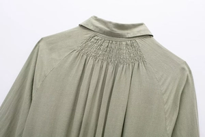 Close-up of sage green linen blend shirt dress featuring smocked back pleats and collar