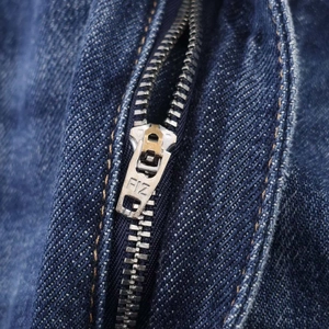 Macro view of a durable metal zipper with brand engraving on dark blue denim fabric