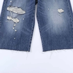 Detail view of classic blue washed denim jeans featuring heavy distressed ripped knee effect