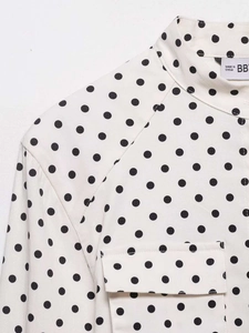 Close-up detail of white polka dot blouse showing collared neck and fabric texture