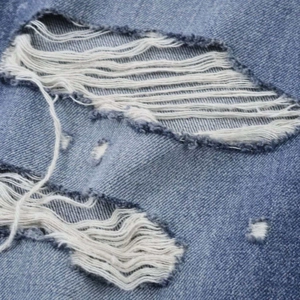 Close-up of distressed denim texture with ripped hole details on mid-waist blue jeans
