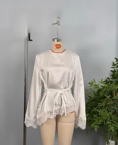 Detailed view of white satin blouse with delicate lace trim on hem and cuffs