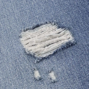 Detailed close-up of distressed blue denim fabric with white frayed ripped hole detail