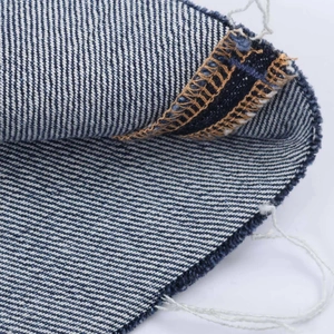 Macro view of blue denim fabric with contrast orange stitching and raw edge detail