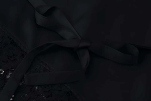 Detail of elegant black satin bow tie and intricate lace trim on women's chiffon blouse