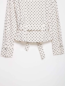 Close-up of white polka dot peplum shirt with belted waist and long sleeves details