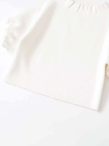 Close-up of white knit top featuring a unique pleated stand collar and fine texture
