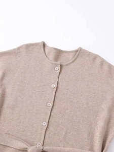 Close-up of oatmeal knitted cardigan with round neck, buttons and drawstring waist tie