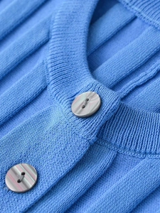 Detail of blue knit cardigan featuring pleated texture and marble pattern buttons