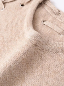 Close-up of beige knitted vest featuring ribbed round neck and metal eyelet lace-up detail