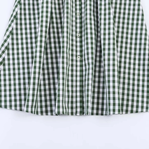 Close-up of green gingham plaid fabric dress with white buttons and pleated details