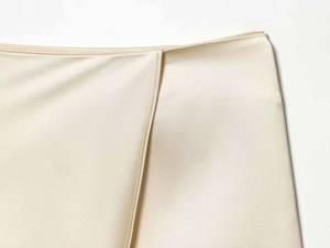 Macro detail of champagne satin skirt with cross-over waist and premium silk texture