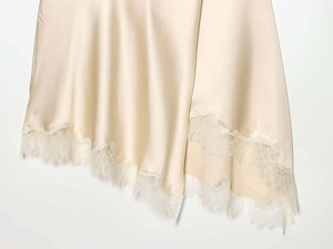 Detail of champagne satin skirt featuring delicate white eyelash lace hem and uneven cut