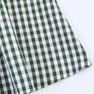 Close-up of green and white gingham fabric texture with fine stitching on dress hem