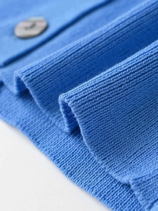 Macro shot of royal blue ribbed knit texture and grey button detail on the stylish cardigan