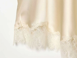 Close-up of champagne satin fabric with delicate eyelash lace hem and floral embroidery